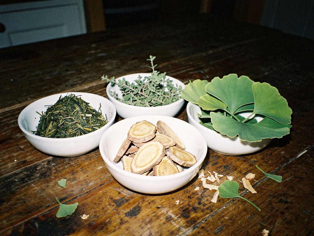 Raw botanicals in small bowls: tea leaves, bacopa, rhodiola root and ginkgo leaves