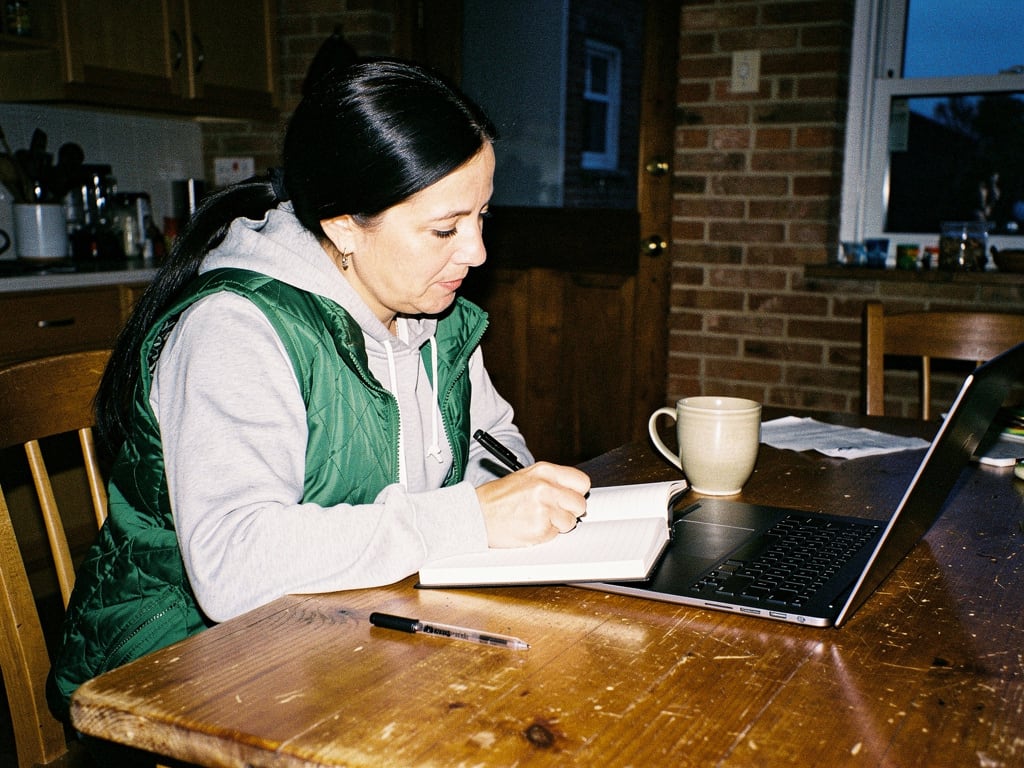 A woman writing ideas in a notebook beside her laptop